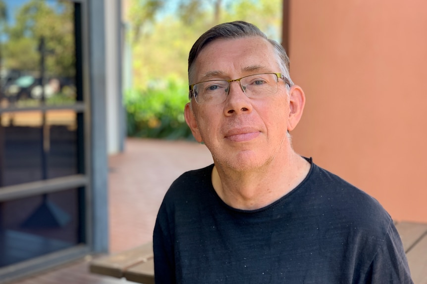 A man wearing glasses and a dark shirt looks thoughtful