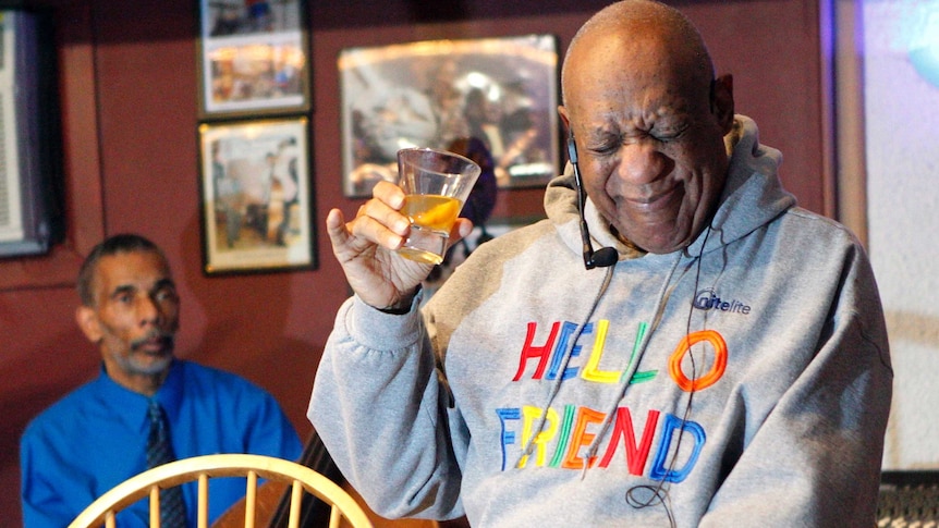Bill Cosby holds a shot glass and screws up his face during a performance.