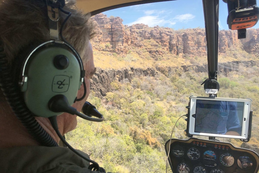 Peter Veth looks out over rocky cliffs and trees from the cockpit of a helicopter.