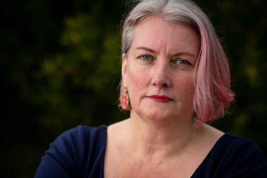 A woman with pink and white hair looks sternly at the camera
