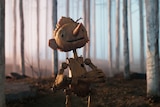 An animated wooden figure resembling a puppet with a long nose stands smiling in a barren wooded landscape.