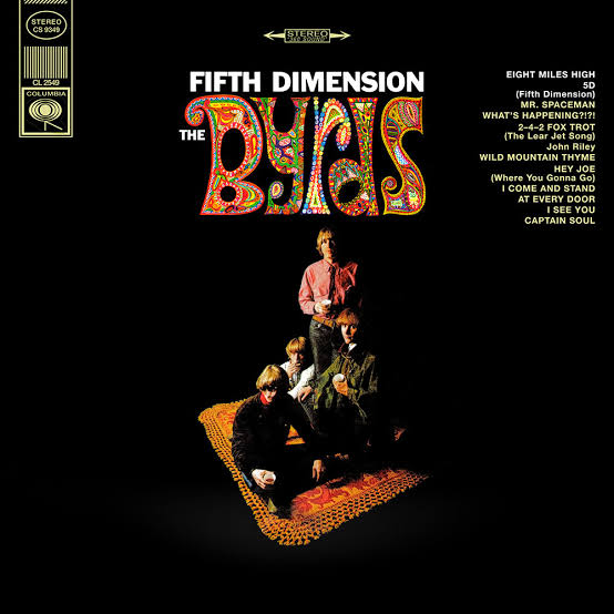 The band members sit on a rug surrounded by darkness