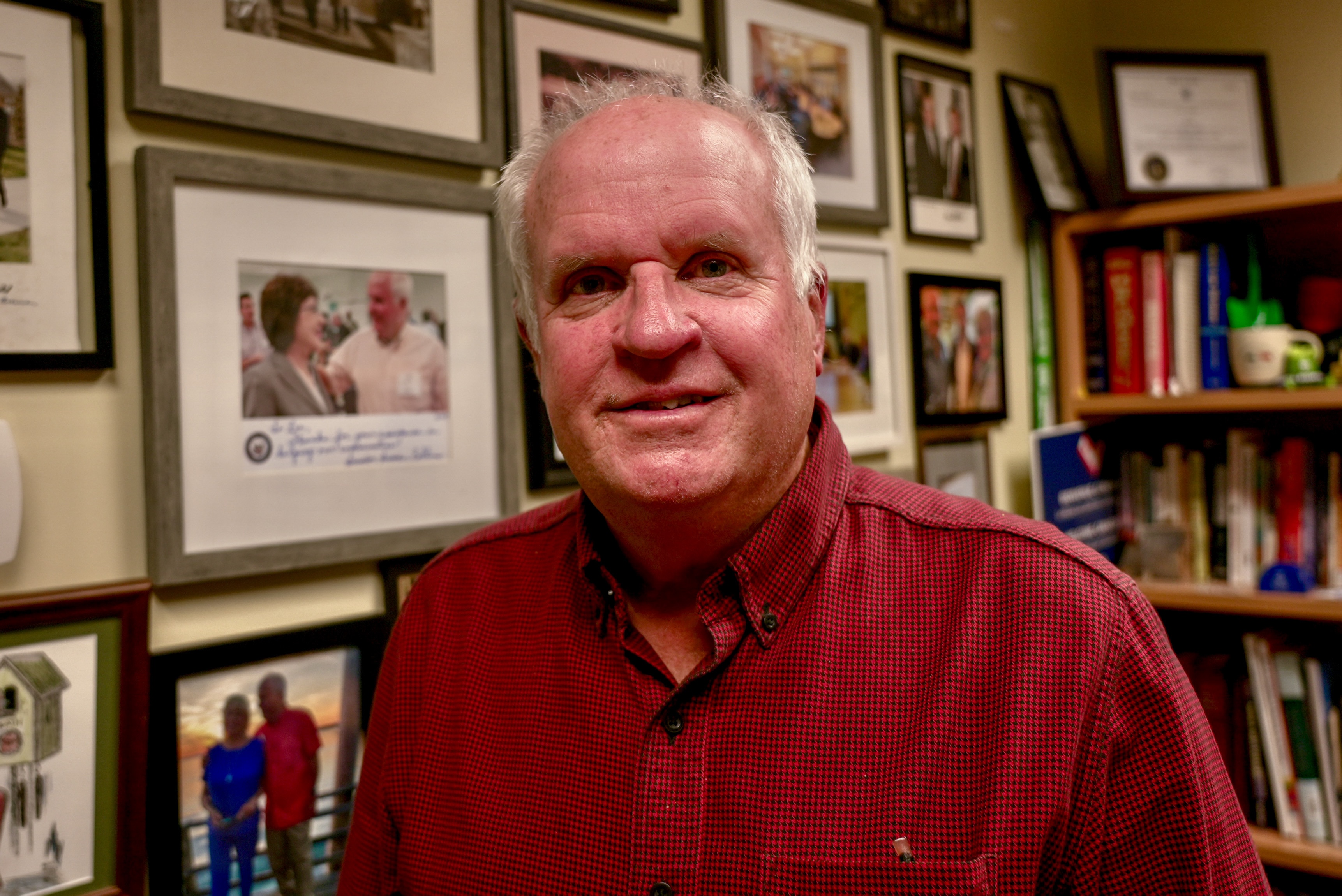Lee Umphrey stands in front of a wall displaying framed photos of politicians.