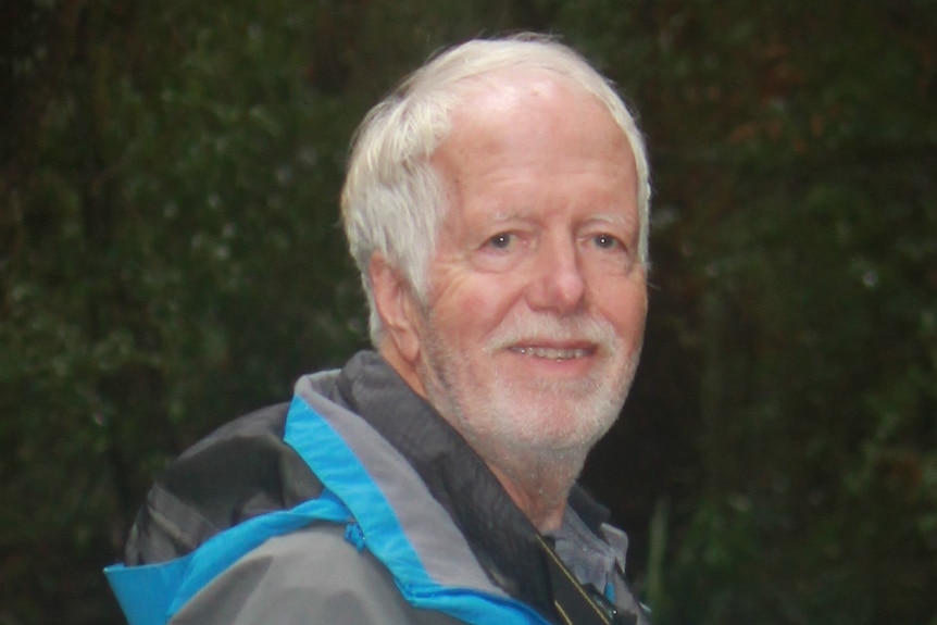Photograph of a man with white hair and a beard smiling and wearing a rain jacket