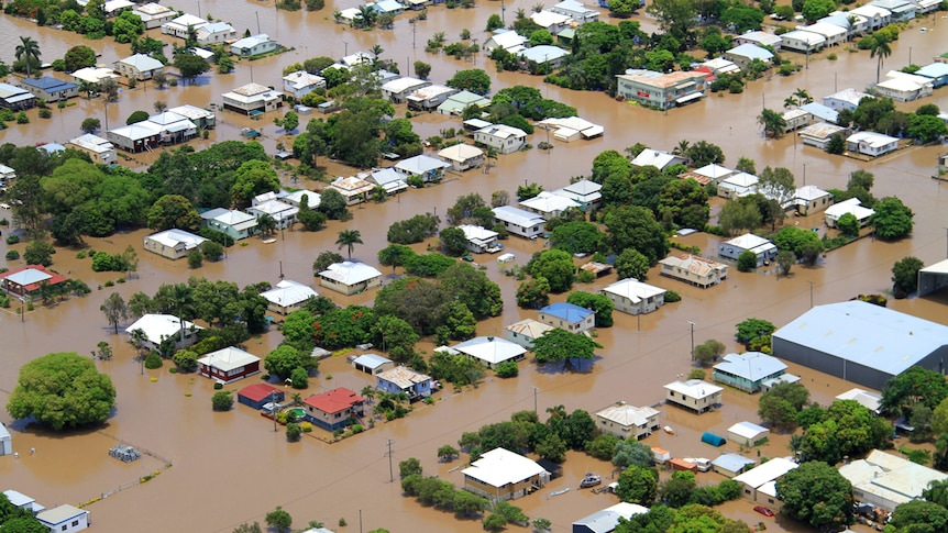 Aerial photograph of houses surrounded by brown muddy flood waters.