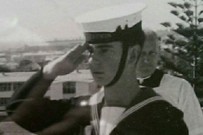 Black and white photo of teenage boy in naval uniform saluting
