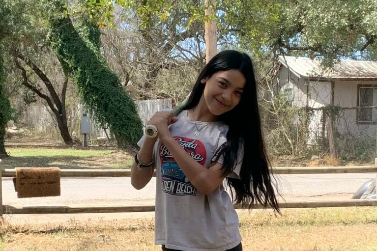 A young girl poses with a baseball bat over her shoulder.