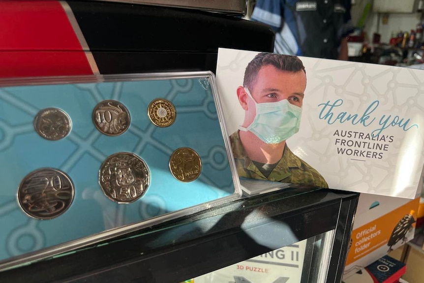A group of Australian coins in a blue frame, next to a bag with a person wearing a mask.