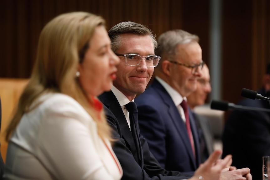 NSW Premier Dominic Perrottet smiles at Qld Premier Annastacia Palaszczuk with PM Albanese in the background. All are seated.