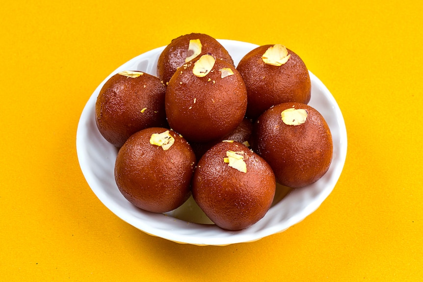 Round sugar syrup coated dough balls (gulab jamun) on a yellow background.