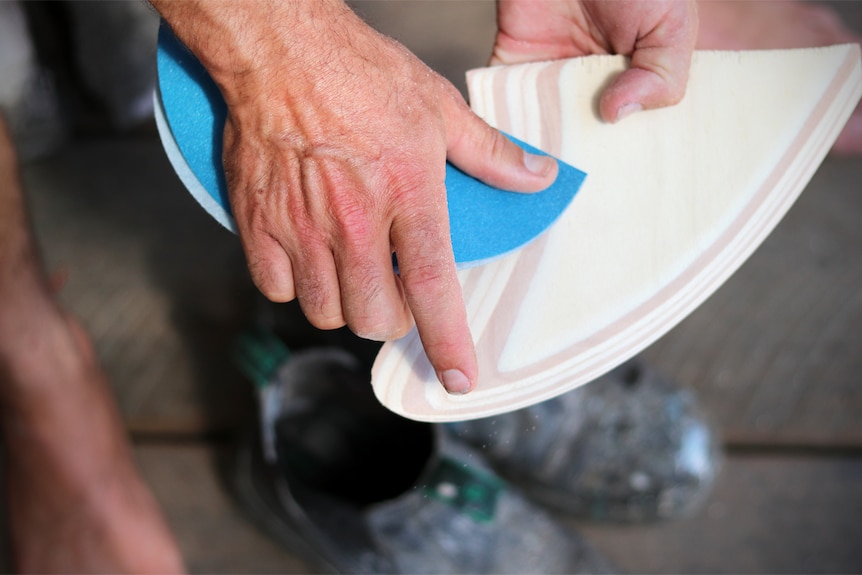 Closeup photo of Dave Porter sanding a wooden fin.