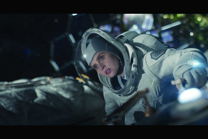 Actor Felicity Jones in a spacesuit adjusting a spaceship in the sci-fi movie The Midnight Sky