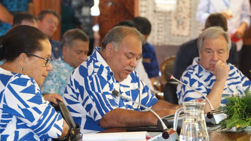 Three people wearing matching blue and white shirts sit at a conferences table speaking into microphones.