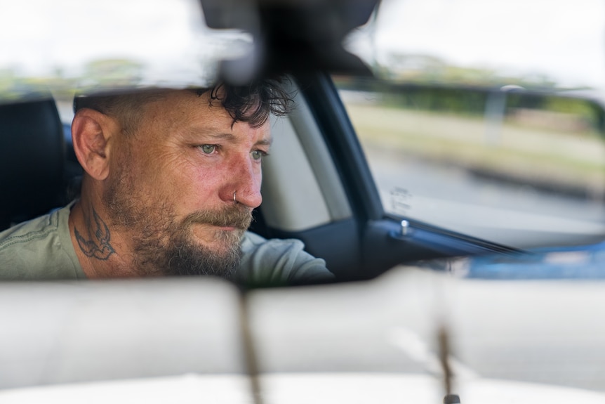 A man's face is seen in a rear-view car mirror.