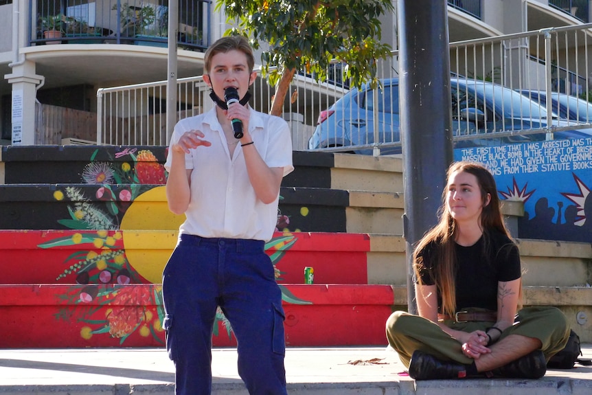 A young woman speaks into a microphone while another woman looks on. 