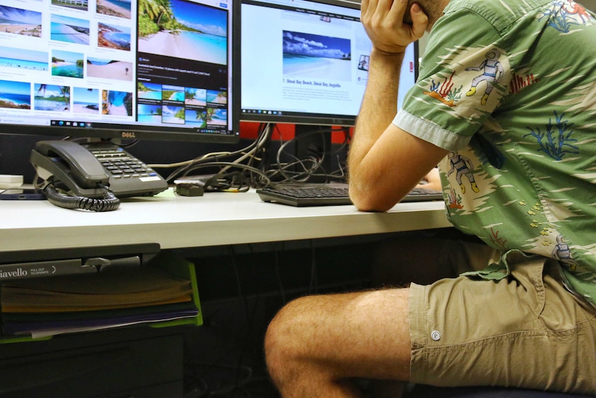 A man browses on an office computer in shorts.