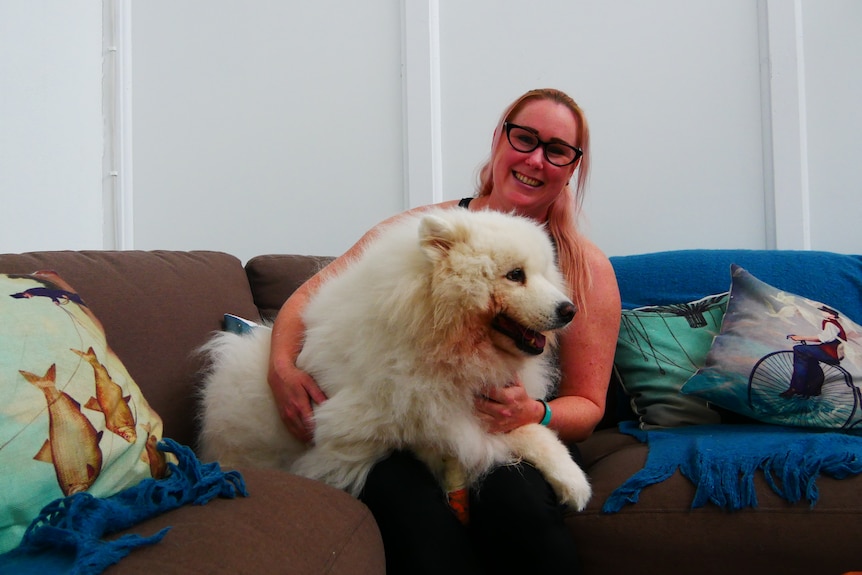 A woman hugs a large fluffy white dog on a colourful couch