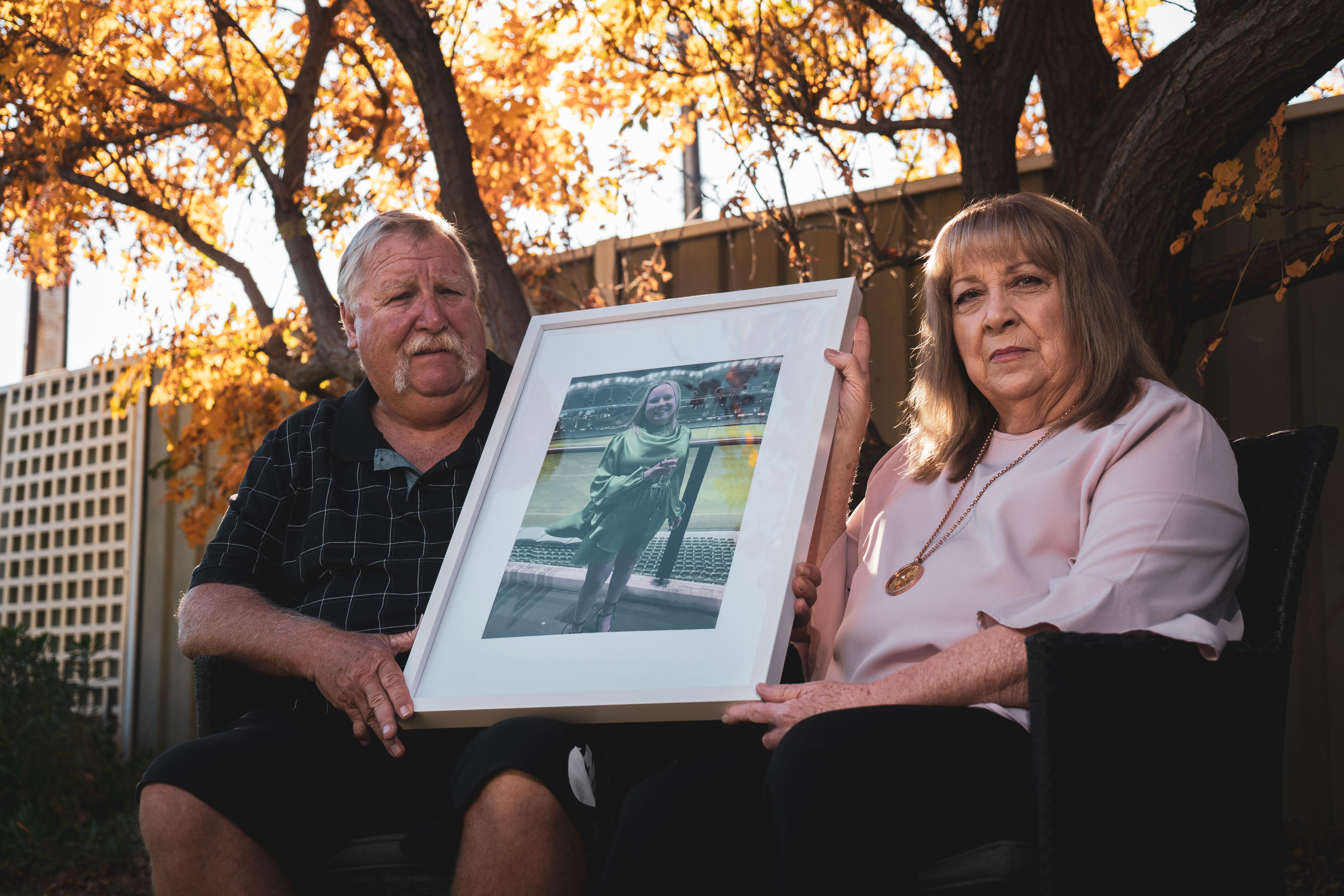 A man and woman hold a framed photo of their daughter