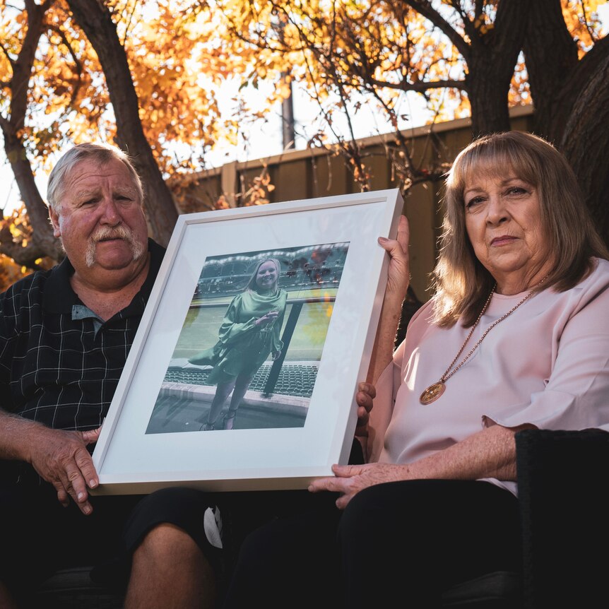 A man and woman hold a framed photo of their daughter