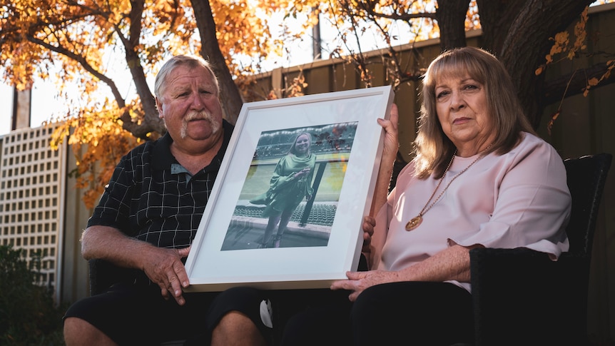 A man and woman hold a framed photo of their daughter