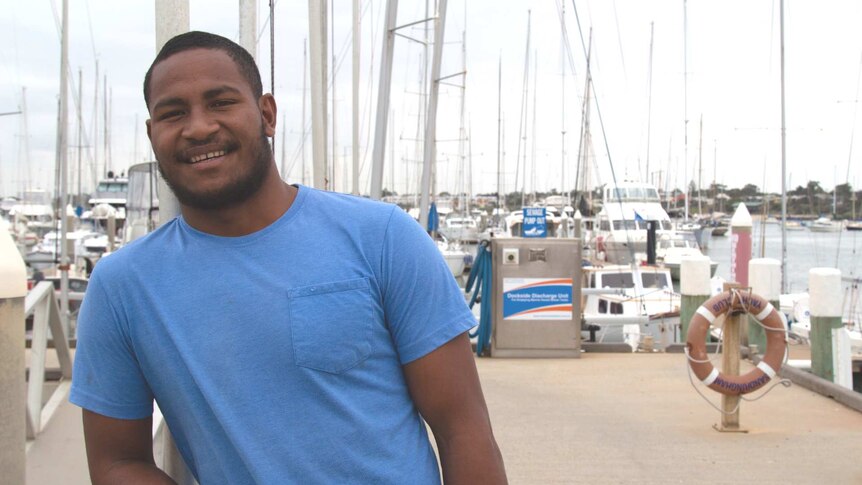 Man standing at the docks smiling in a blue shirt.