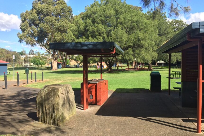 A barbecue area opening onto a green park, with a playground in the background.