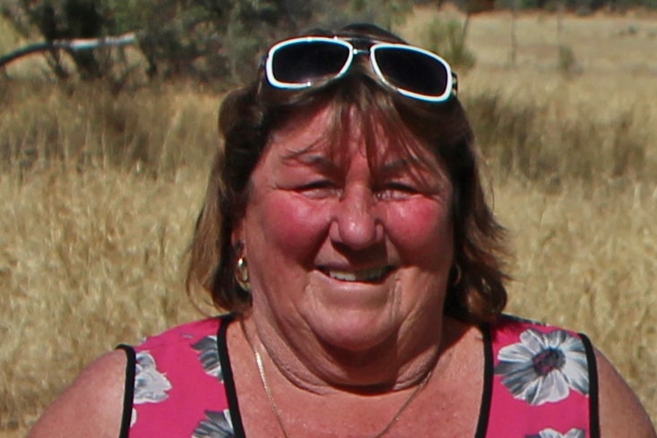 A lady in a pink singlet smiles at the camera.