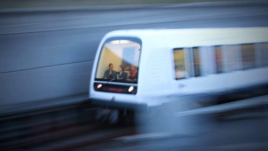 The front of a white train is captured mid-motion, as passengers sit in the front of it where a driver would normally be.