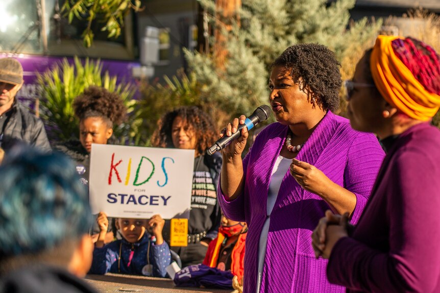 Stacey Abrams speaks to a group of supporters wearing a purple jacket