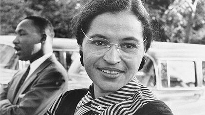 Rosa Parks leans against a car and smiles with Martin Luther King Jr in the background.