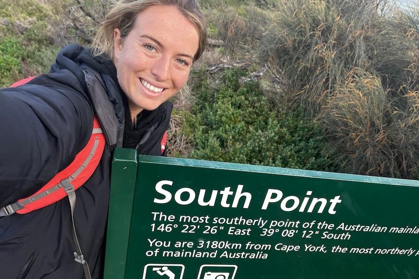 Selfie photo of woman with sign reading 'South Point - the most southerly point of Australia's mainland'.