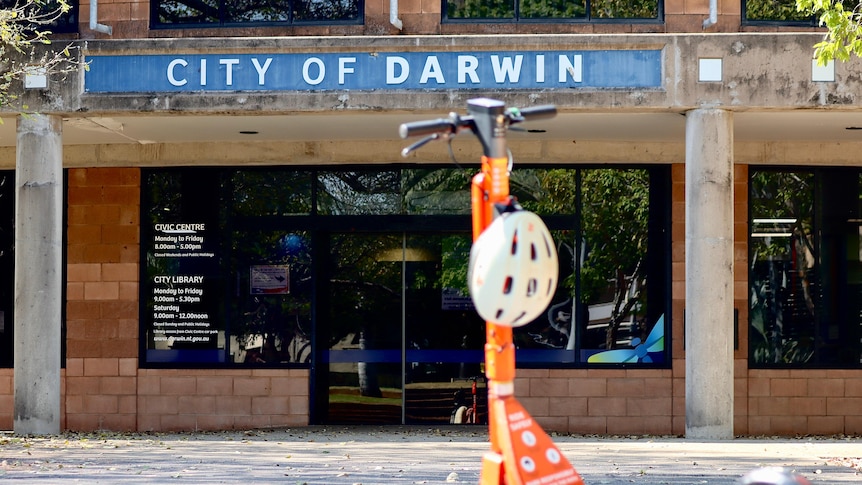 An e-scooter with helmet attached stands upright in front of a council building