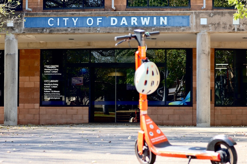 An e-scooter with helmet attached stands upright in front of a council building
