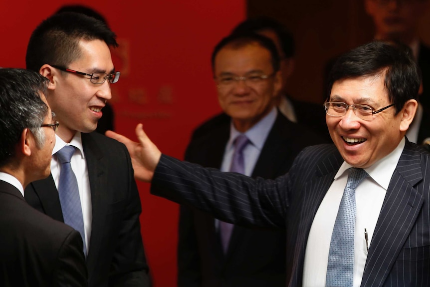 A group of Hong Kong businessmen in suits greet each other in a read room