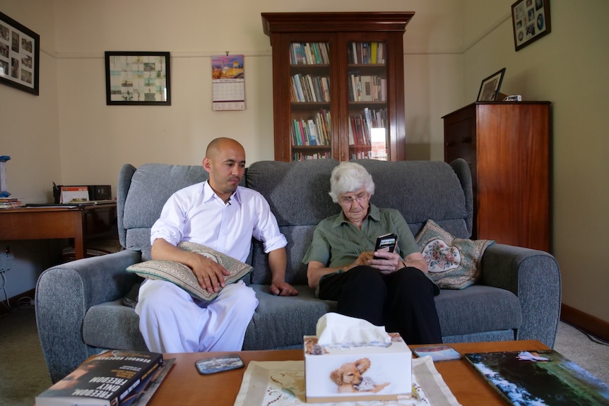 A man and woman sit next to each other on a couch looking at photos on a phone.