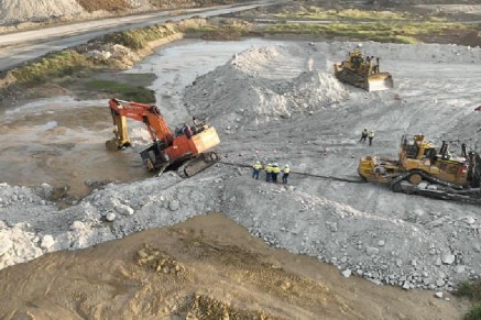 An excavator sinking into mud at a mine.  A large dozer is being used to drag it out.