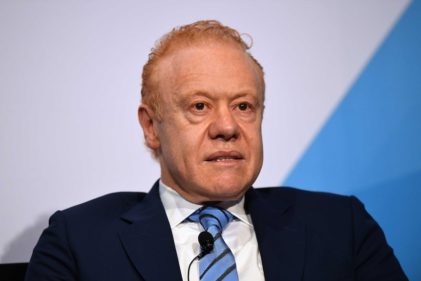 Anthony Pratt wears sits in a suit, against a plain, indoors background, with a neutral expression