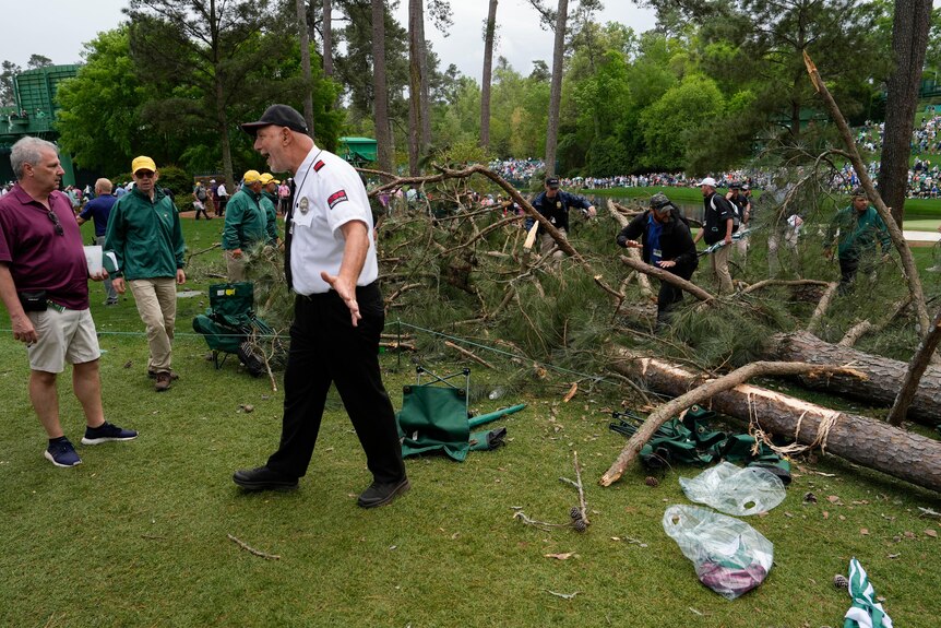 A security guard ushers people away as others sift through a massive fallen branch on a golf course