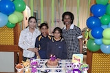 A family stand in front of a birthday cake. 