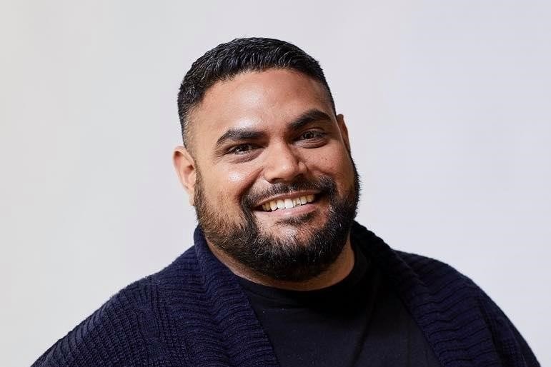 A man smiles for a portrait in front of a plain background, and reflects on his interracial relationship.