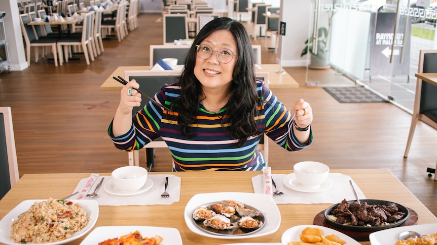Jennifer Wong holding chopsticks, sits at a table eating a range of Chinese dishes. 