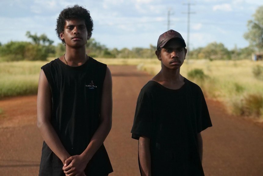 Two boys pose for a photo along a dirt road in an outback setting