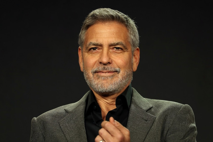 A man in a suit smiles as he sits in front of a black background.