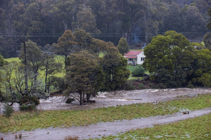 A raging river flows past a small cottage on a hill.