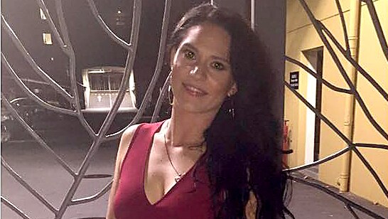 Jessica Carter poses for a photo at night wearing a dark red top and white pants and holding a small handbag.