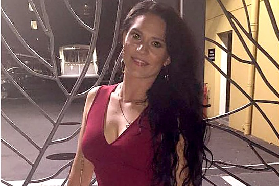 Jessica Carter poses for a photo at night wearing a dark red top and white pants and holding a small handbag.