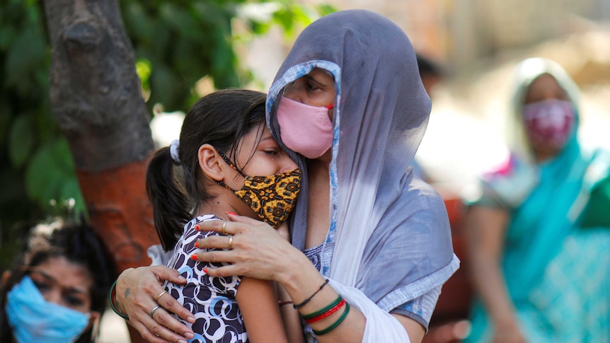 A woman wearing a hijab and a mask holds onto a young girl crying while wearing a mask