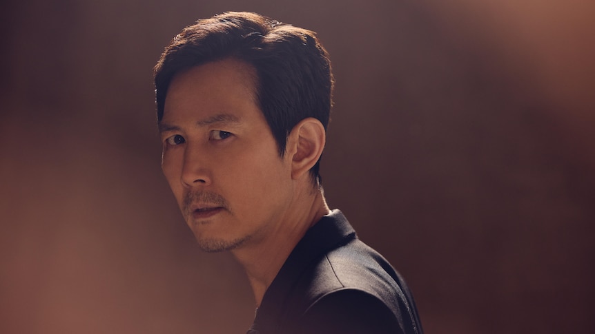Lee Jung-Jae looks over his shoulder in a stylised portrait shot, a serious look on his face