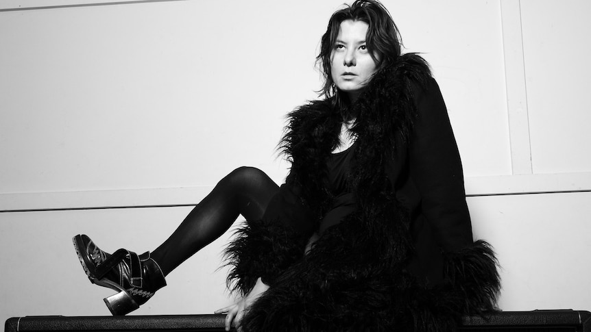 Black and white photo of the lead singer for Full Flower Moon Band, sitting on guitar amplifiers