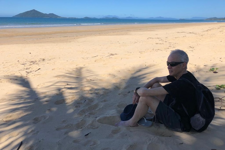 A man on a beach under a palm tree.